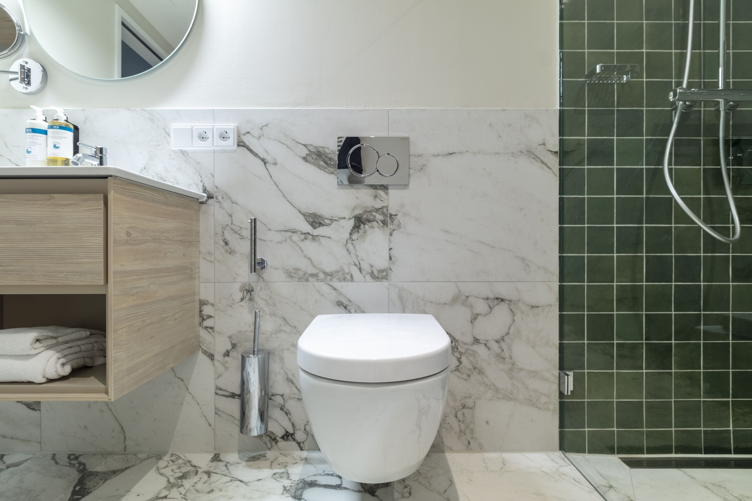 Ein modernes Badezimmer mit Marmorboden, Toilette in Weiß, Waschtisch aus Holz mit Handtüchern und einer Duschkabine aus Glas.