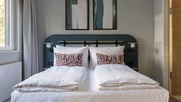 A double bed with white linens and patterned pillows, a dark headboard, and two abstract paintings on the wall.