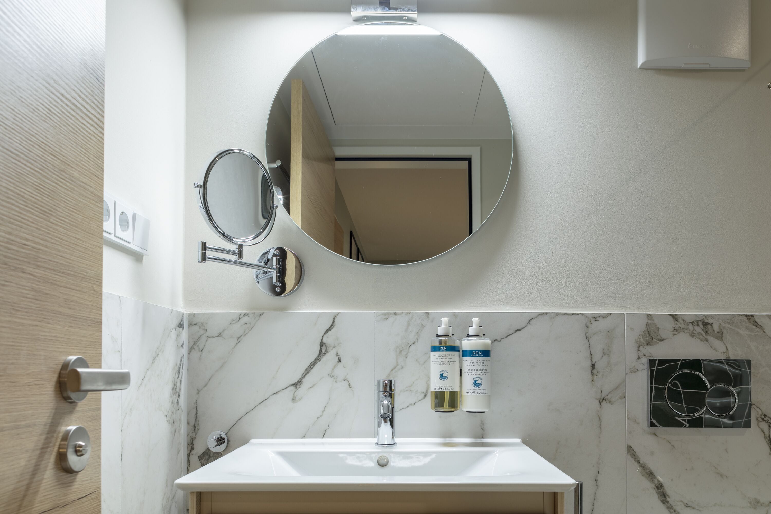 A bathroom with a marble sink, a round mirror, and two toiletry bottles.