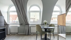 Ein moderner Raum mit Esstisch, zwei Stühlen, einer Blumenvase und großen, bogenförmigen Fenstern mit Vorhängen.