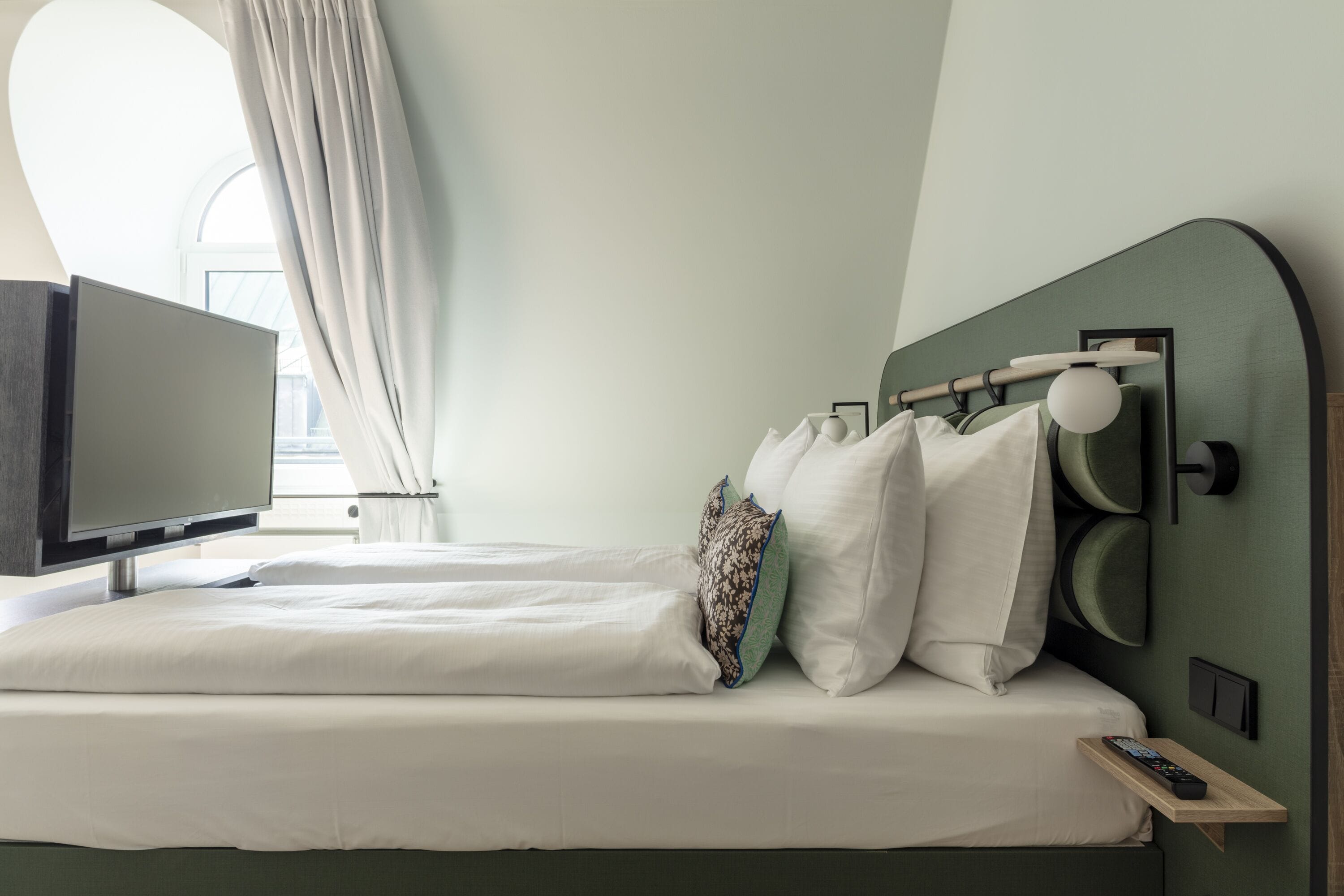 Una habitación de hotel moderna con una cama, un televisor y un ventanal con cortinas.
