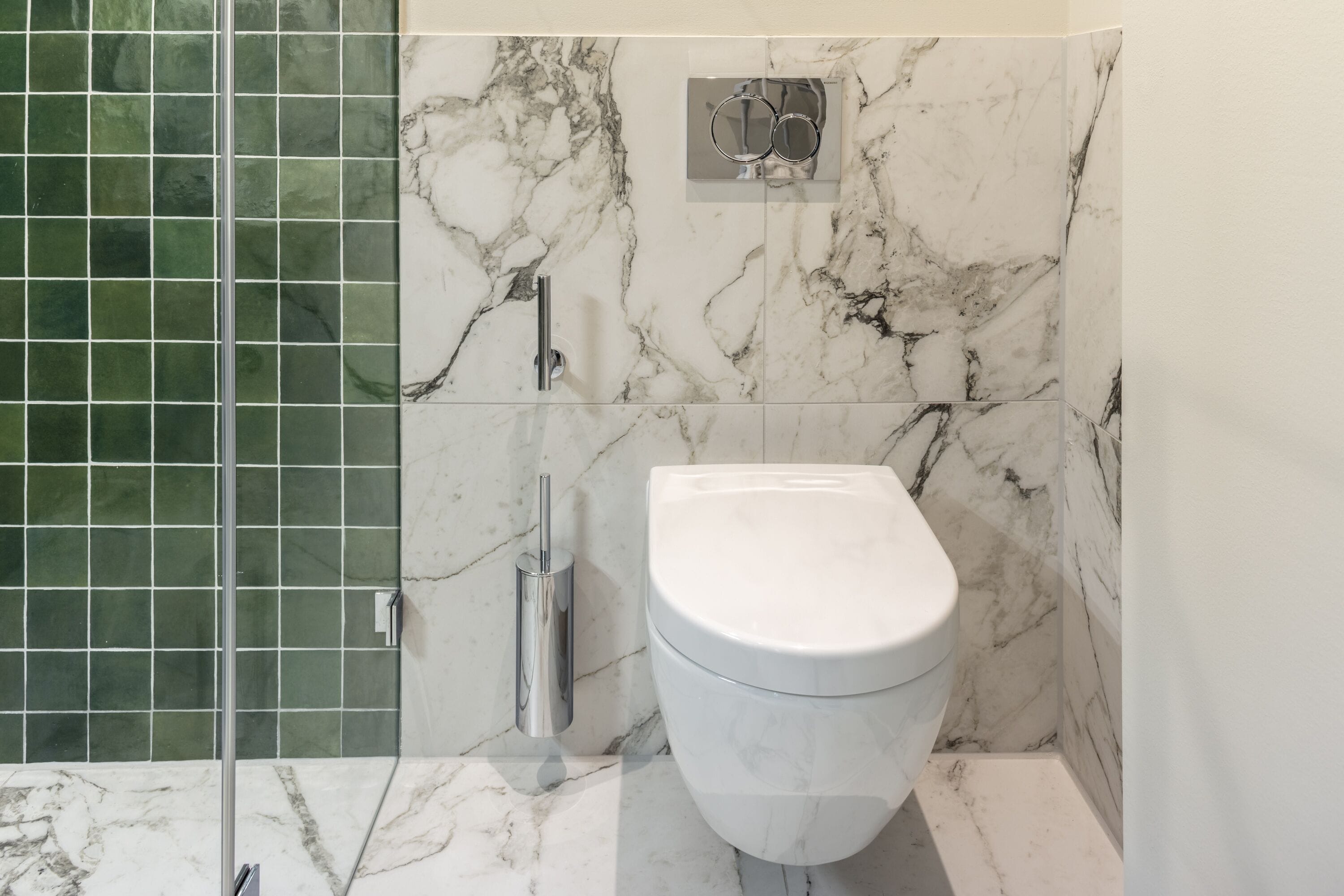 Une salle de bain avec des toilettes blanches, une cabine de douche en verre et un mur en marbre.