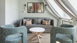 Ein modernes Wohnzimmer mit einem grauen Sofa, zwei passenden Sesseln, einem weißen Couchtisch und abstrakter Kunst an der Wand.
