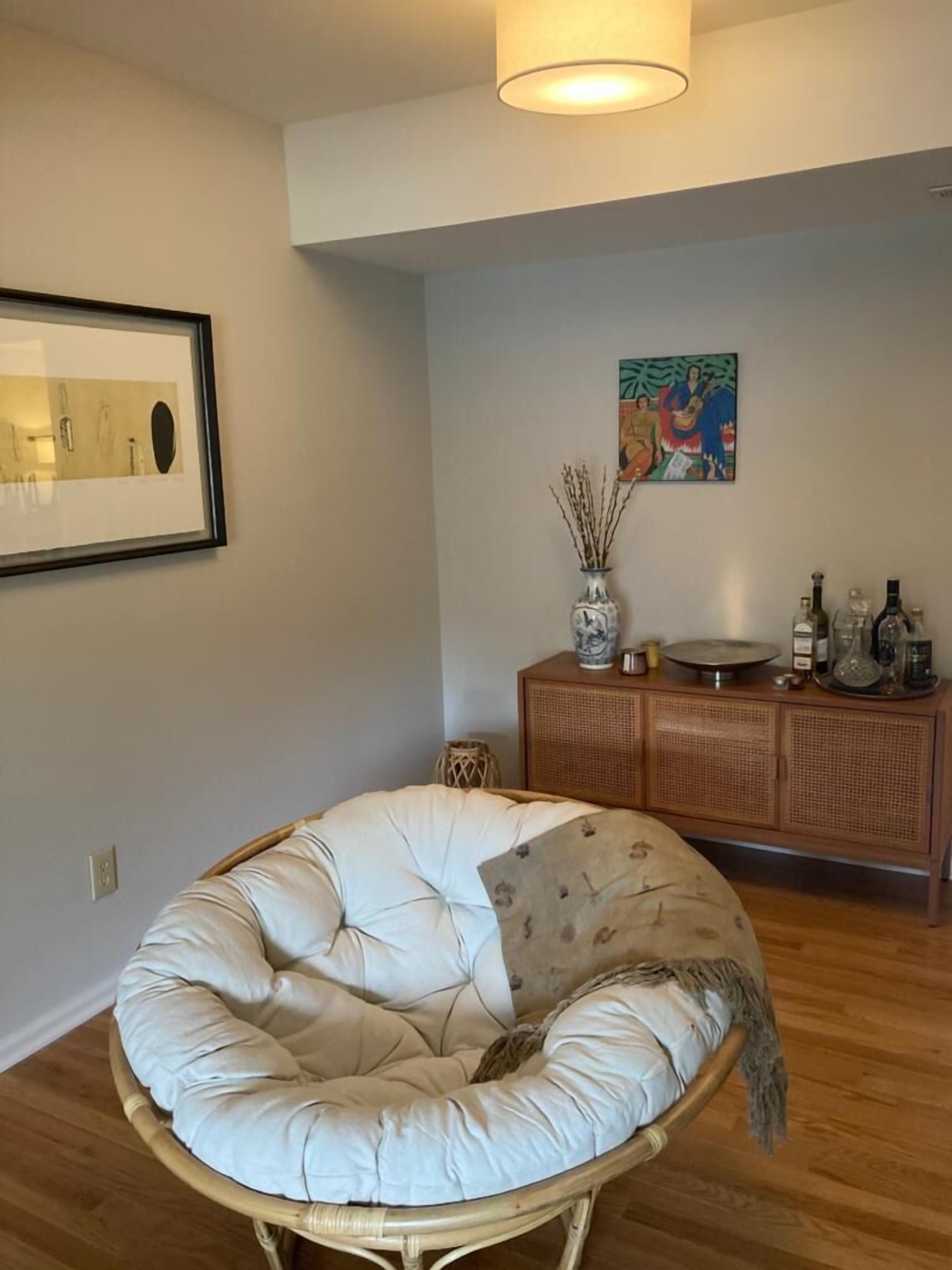 A room with a round, cushioned seating area, a wooden cabinet with decorative items, and a framed artwork on the wall.