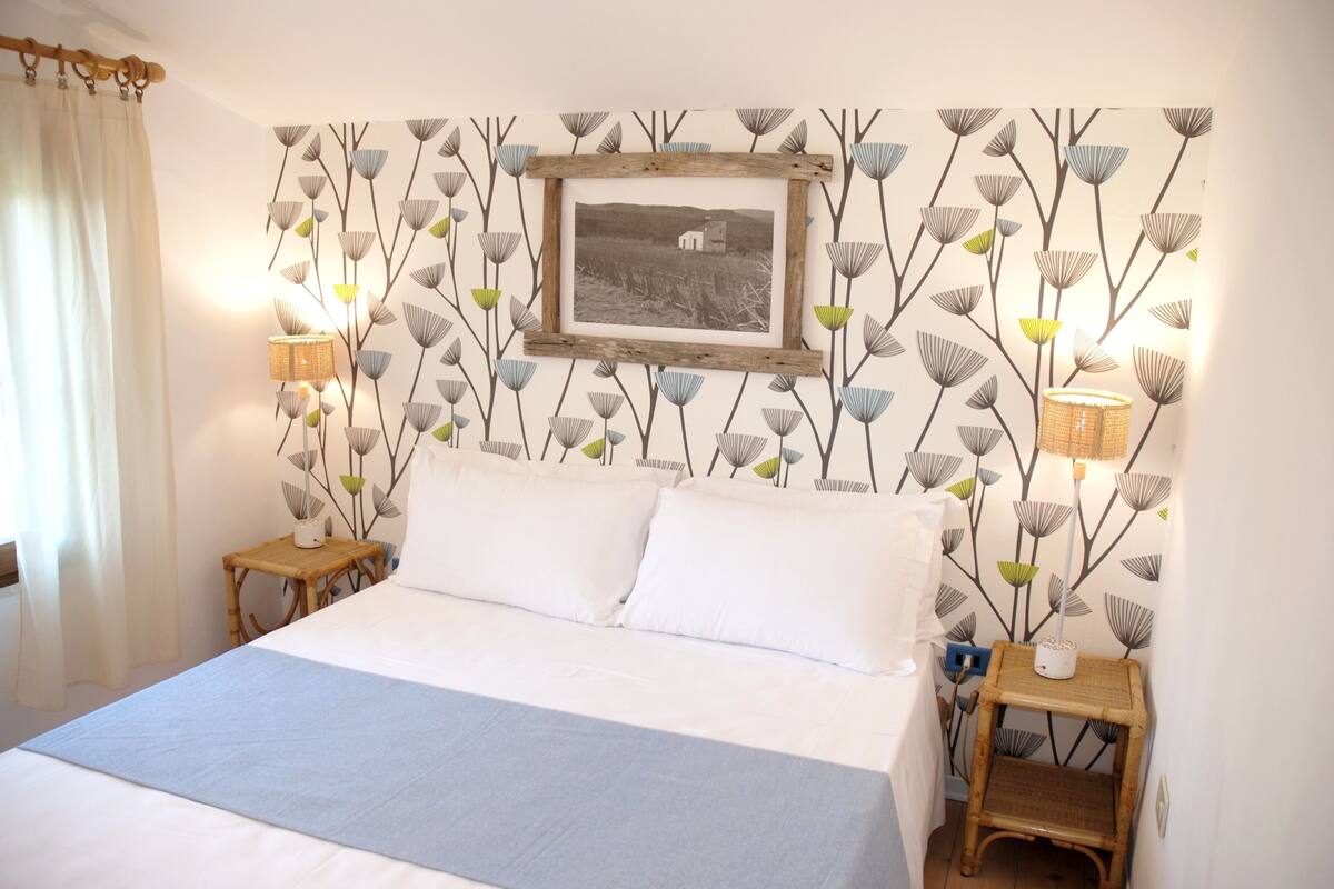 A bedroom with a bed, two nightstands, a lamp, and a wall-mounted picture.