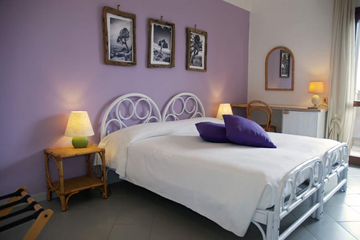 A bed with a white mattress and purple pillows, a bedside table with a lamp, and three framed pictures on the wall.