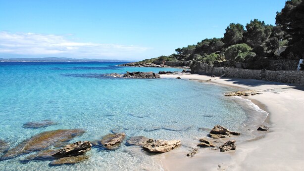 A clear beach with visible rocks and a stone wall. - Hotel Galman (Carloforte)