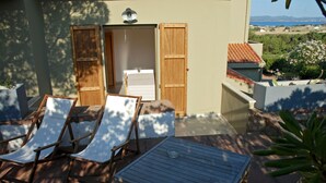 A patio with two lounge chairs and a table, a wooden door, and a view of the sea. - Hotel Galman (Carloforte)