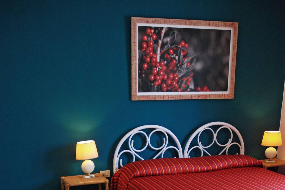 A bedroom with a bed, two bedside tables with lamps, a chair, and a framed picture on the wall.