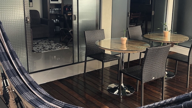 A modern outdoor seating area with a glass table and chairs, a potted plant, and a view of the interior space. - Pousada da Paz (Curitiba)