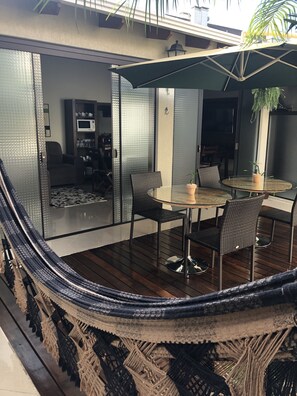 A modern outdoor seating area with a glass table and chairs, a potted plant, and a view of the interior space. - Pousada da Paz (Curitiba)