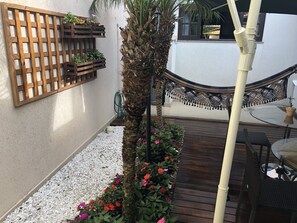 A wooden deck with a hammock, a wooden planter with flowers, and a palm tree. - Pousada da Paz (Curitiba)