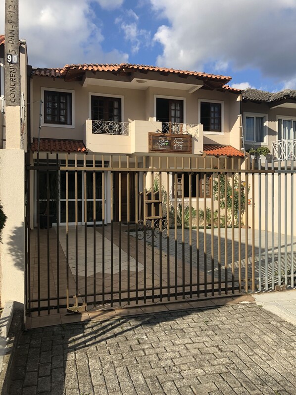 A gated entrance to a building with a tiled roof, a sign indicating a spa and restaurant, and a paved driveway. - Pousada da Paz (Curitiba)