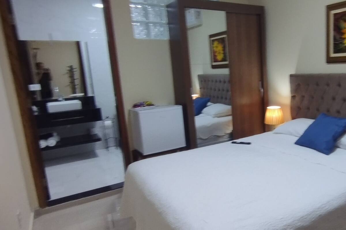 Habitación de hotel con una cama grande, dos lámparas de noche, un espejo y un cuadro con motivos florales en la pared.