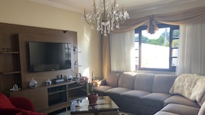A living room with a large flat-screen TV, a chandelier, a sofa, and a red armchair. - Pousada da Paz (Curitiba)
