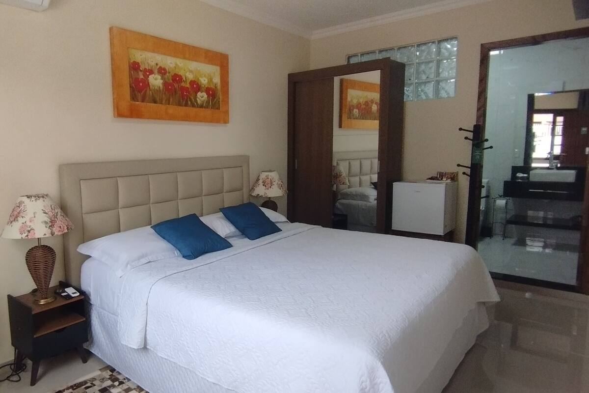 Un dormitorio con cama, mesitas de noche, una lámpara y un cuadro en la pared.