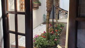 A wooden door with a glass panel, leading to a courtyard with a palm tree, potted plants, and a small garden area with pebbles and flowers. - Pousada da Paz (Curitiba)