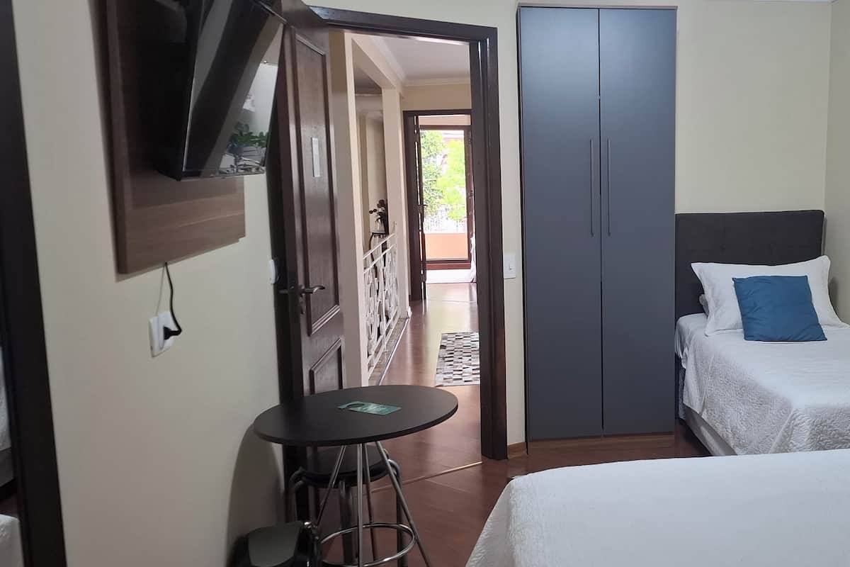 Un dormitorio con dos camas, un televisor montado en la pared, un armario y una mesita.
