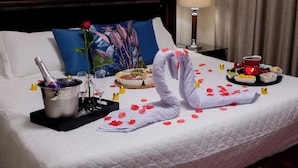 A neatly made bed with a bouquet of red roses, a champagne bottle, and a tray of food and drinks. - Pousada da Paz (Curitiba)