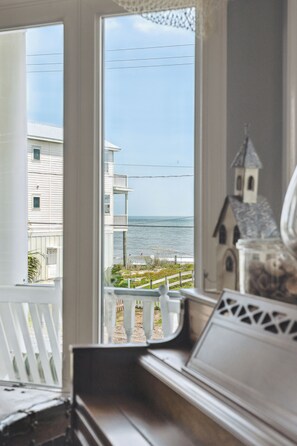 Enjoy the serene ocean view from this stylish room, featuring a piano, decorative house model, and comfortable chair.