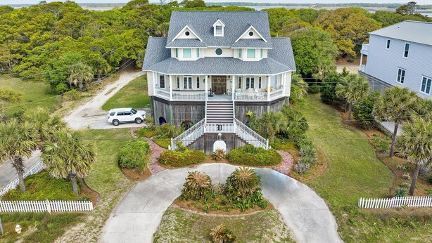 A large, two-story house with a front porch, a driveway, and a white picket fence. - Private Pool, Ocean View, Beach Access Across Street - Castle By The Sea (Folly Beach)