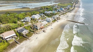 An aerial view of a coastal town with beachfront properties, a pier, and a lighthouse in the distance. - Private Pool, Ocean View, Beach Access Across Street - Castle By The Sea (Folly Beach)