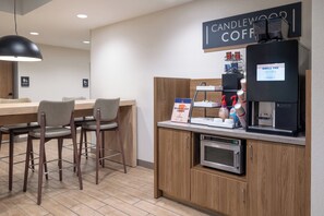Un espace café moderne comprenant une machine à café, une enseigne indiquant « CANDLEWOOD COFFEE » et un panneau affichant le menu.