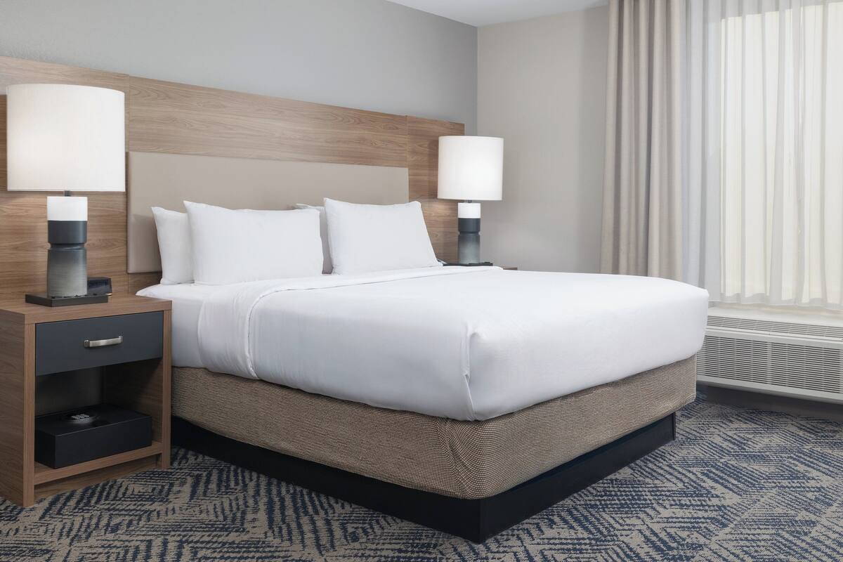 A hotel room with a large bed, two bedside tables with lamps, a wooden headboard, and a patterned carpet.