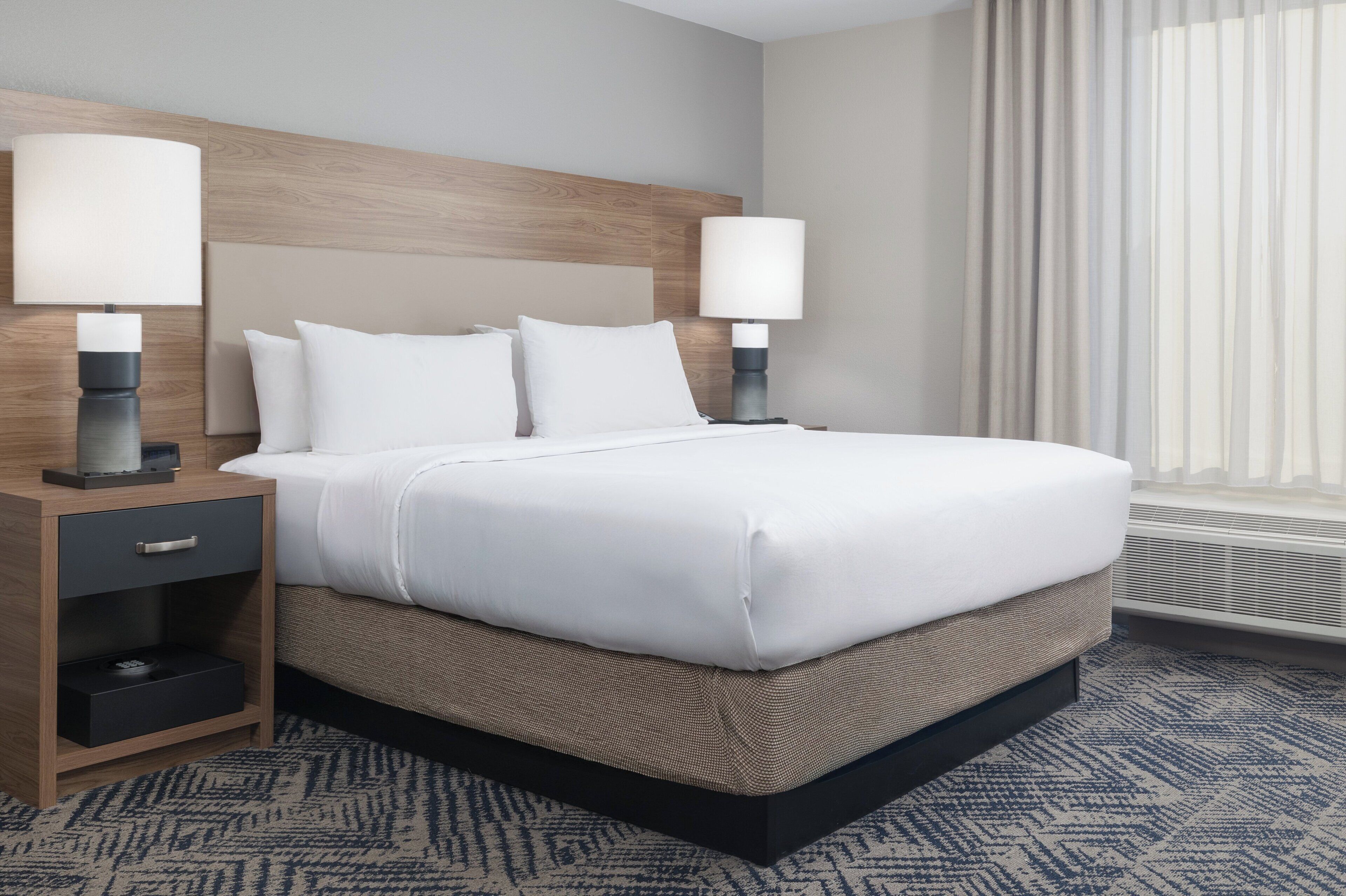 A hotel room with a large bed, two bedside tables with lamps, a wooden headboard, and a patterned carpet.