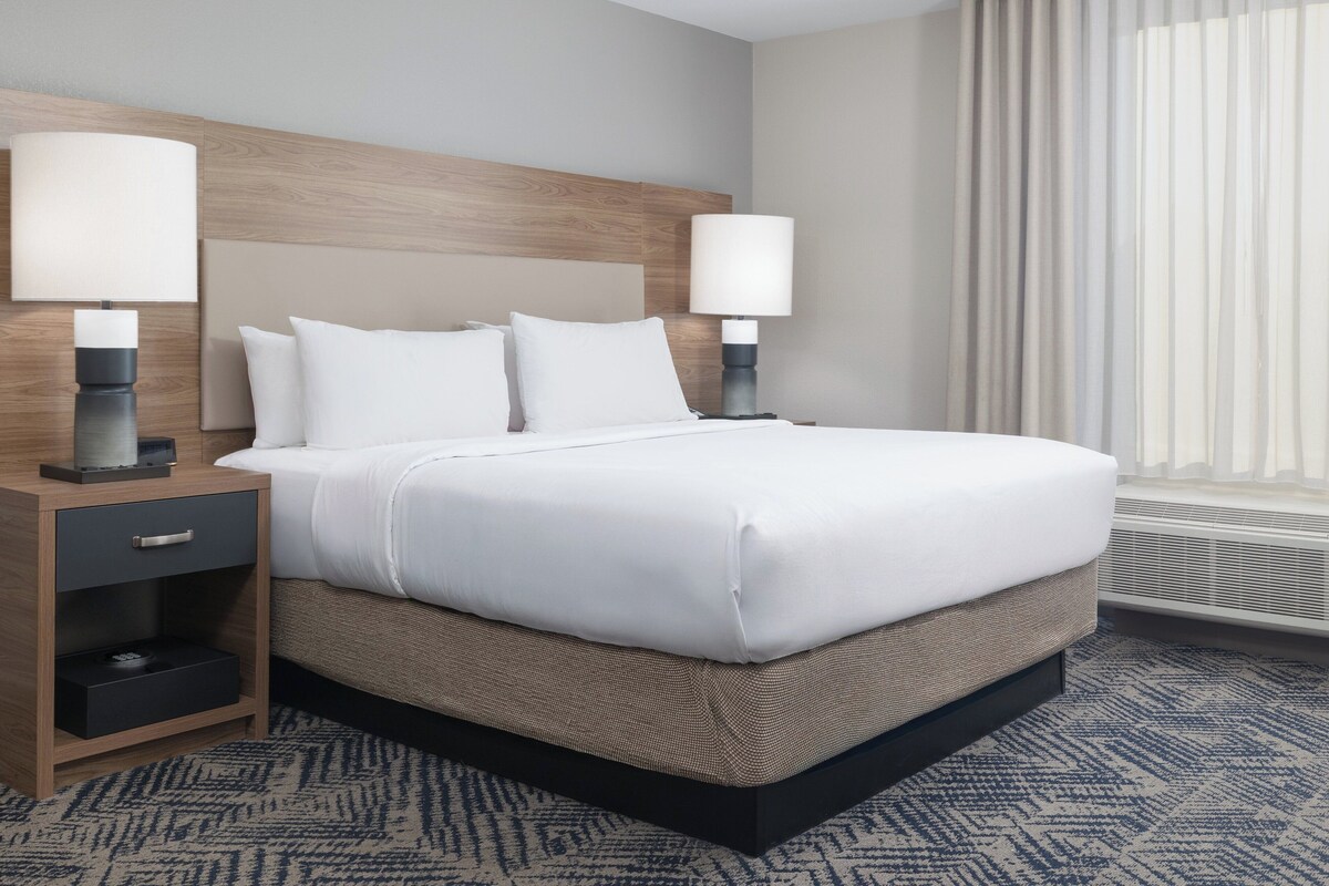 Une chambre d’hôtel avec un grand lit, deux tables de chevet avec des lampes, une tête de lit en bois et une moquette à motifs.