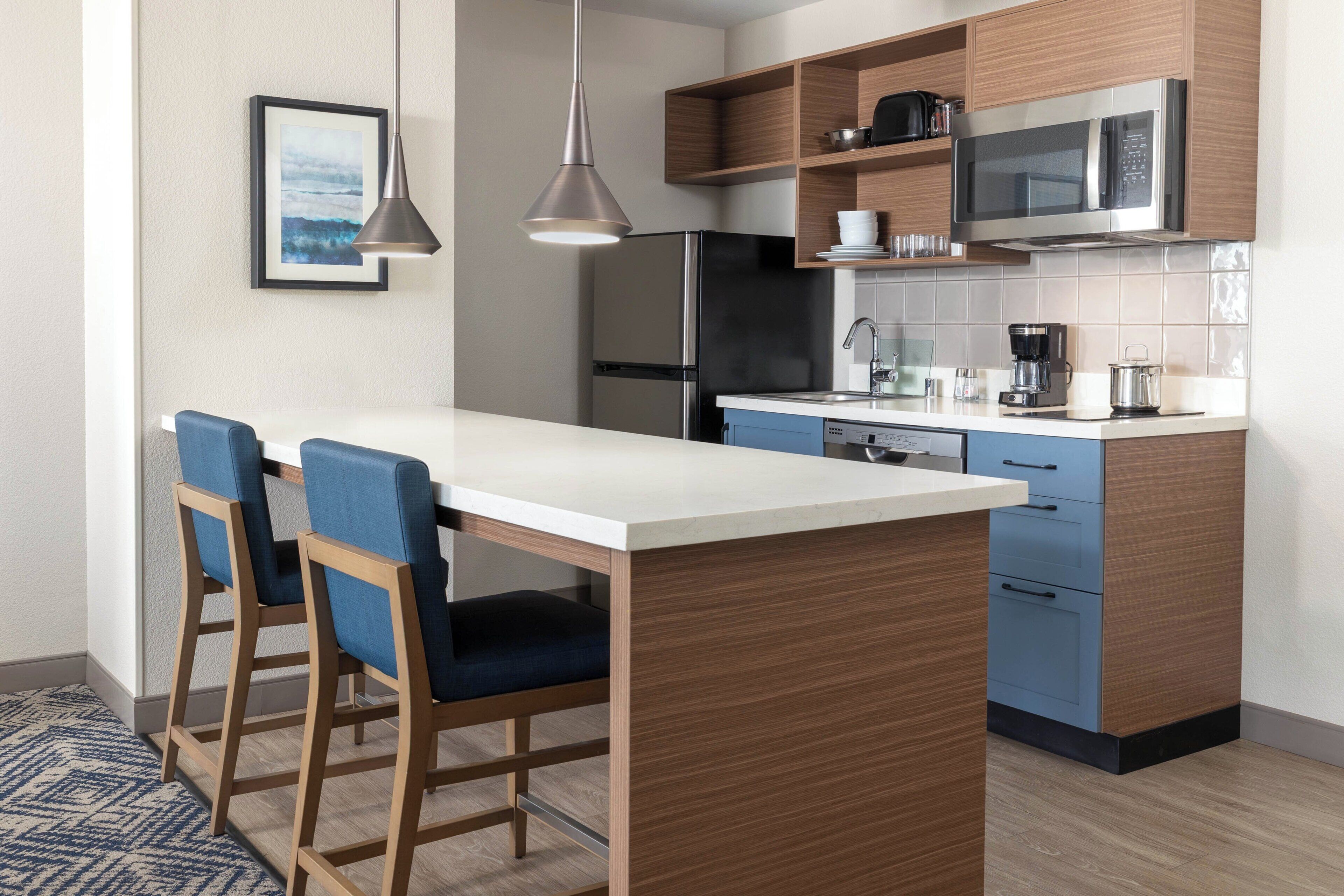 Una cocina moderna con una isla central, taburetes de bar, un refrigerador, un microondas y una cafetera.
