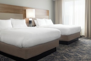 A hotel room with two beds, a nightstand, a lamp, and a large window with curtains. - Candlewood Suites Las Vegas - E Tropicana by IHG (Las Vegas)