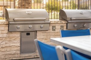 Une cuisine extérieure dotée de deux barbecues encastrés, d’un évier intégré et d’un plan de travail en pierre.