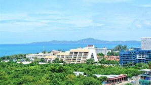 A coastal hotel with multiple buildings, including a prominent white structure with balconies, surrounded by lush greenery and a view of the sea. - 13th Floor sea View Studio (Pattaya)