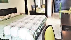 A hotel room with a large bed, a desk, and a chair. There is a mirror on the wall and a door leading to another room. - 13th Floor sea View Studio (Pattaya)
