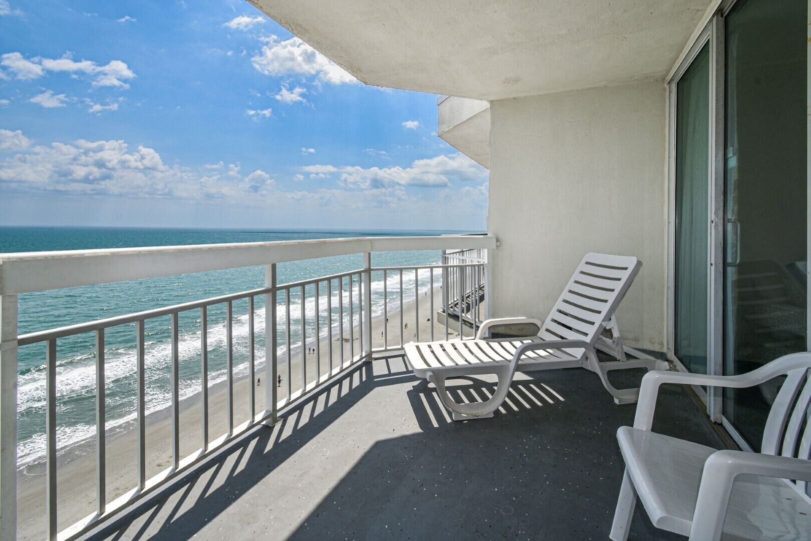 A balcony with white chairs, a glass door, and a view of the ocean.