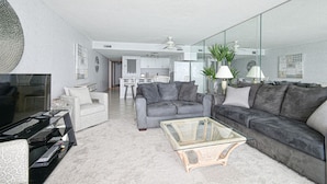 A modern living room with a grey sofa, a glass coffee table, and a TV. - Water's Edge 1511 - Two Bedroom, Two Bathroom, Oceanfront Condo (Garden City Beach)