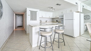 A modern kitchen with white cabinetry, a central island with stools, and a microwave above the island. - Water's Edge 1511 - Two Bedroom, Two Bathroom, Oceanfront Condo (Garden City Beach)