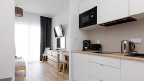 A modern kitchen with white cabinets, a microwave, a kettle, and a coffee maker. There is a wooden dining table with chairs and a small seating area with a sofa and a coffee table. - Wola Chic Brown Studio (Warsaw)