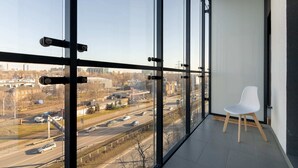 A modern room with large floor-to-ceiling windows, a white chair, and a view of a busy road and buildings. - Wola Chic Brown Studio (Warsaw)