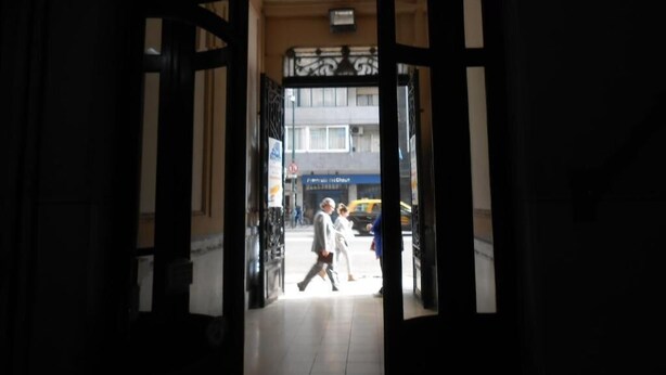 An entrance with a black metal gate and a tiled floor leading to a building with a blue sign. - Hotel San Martin (Buenos Aires)
