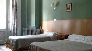 A hotel room with two beds, a wooden headboard, a radiator, a nightstand, and a wall-mounted lamp. - Hotel San Martin (Buenos Aires)