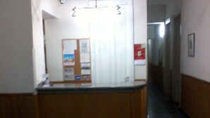 A hallway with a reception desk, a bulletin board, and a door with a poster. - Hotel San Martin (Buenos Aires)