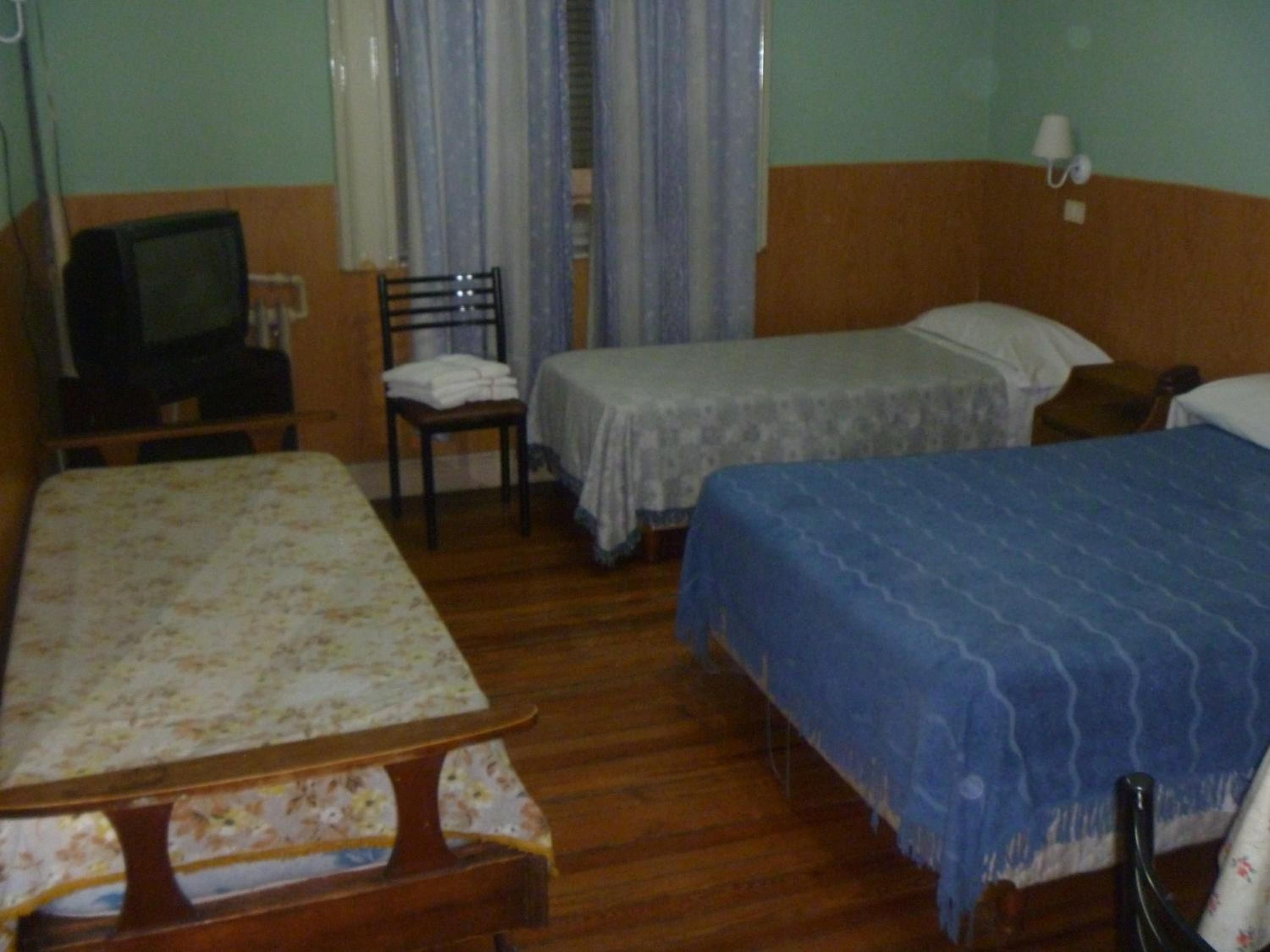 Una camera d'albergo con due letti, una sedia, una televisione e un comodino.