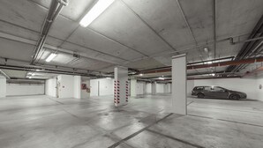 A spacious parking garage with concrete floors and white pillars, featuring a car parked in one of the bays.