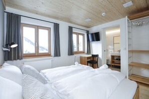 Ein Hotelzimmer mit zwei Betten, einem Schreibtisch, einem Sessel, einem Fernseher und einem sichtbaren Badezimmer durch eine geöffnete Tür.