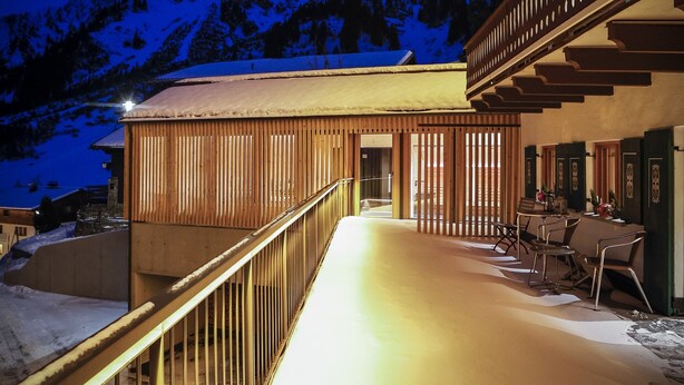 Un bâtiment en bois doté d’un balcon, un sol recouvert de neige et une montagne en arrière-plan.