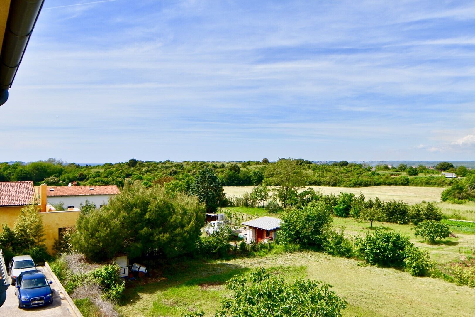 A rural landscape with a house, parked cars, and a field.