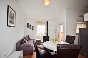 Ein modernes Wohnzimmer mit einer Couch, einem Esstisch mit Stühlen und einem durch eine offene Tür sichtbaren Küchenbereich.
