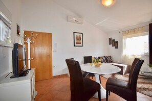 Ein Essbereich mit einem runden Tisch, vier Stühlen, einer Vase mit Blumen und einer Couch mit Kissen.
